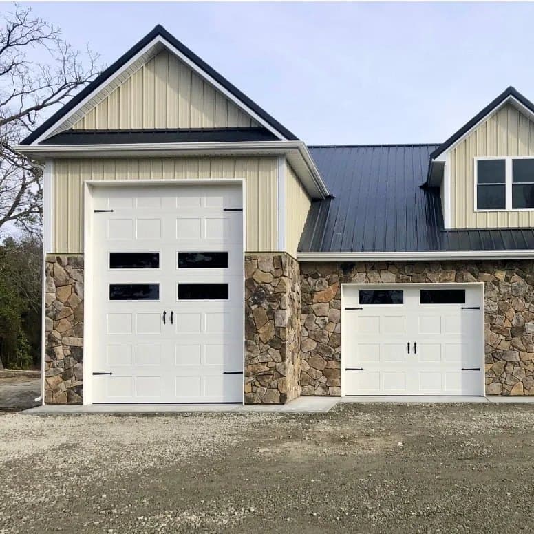 Stone-front garage addition with one tall and one standard white carriage-style garage door