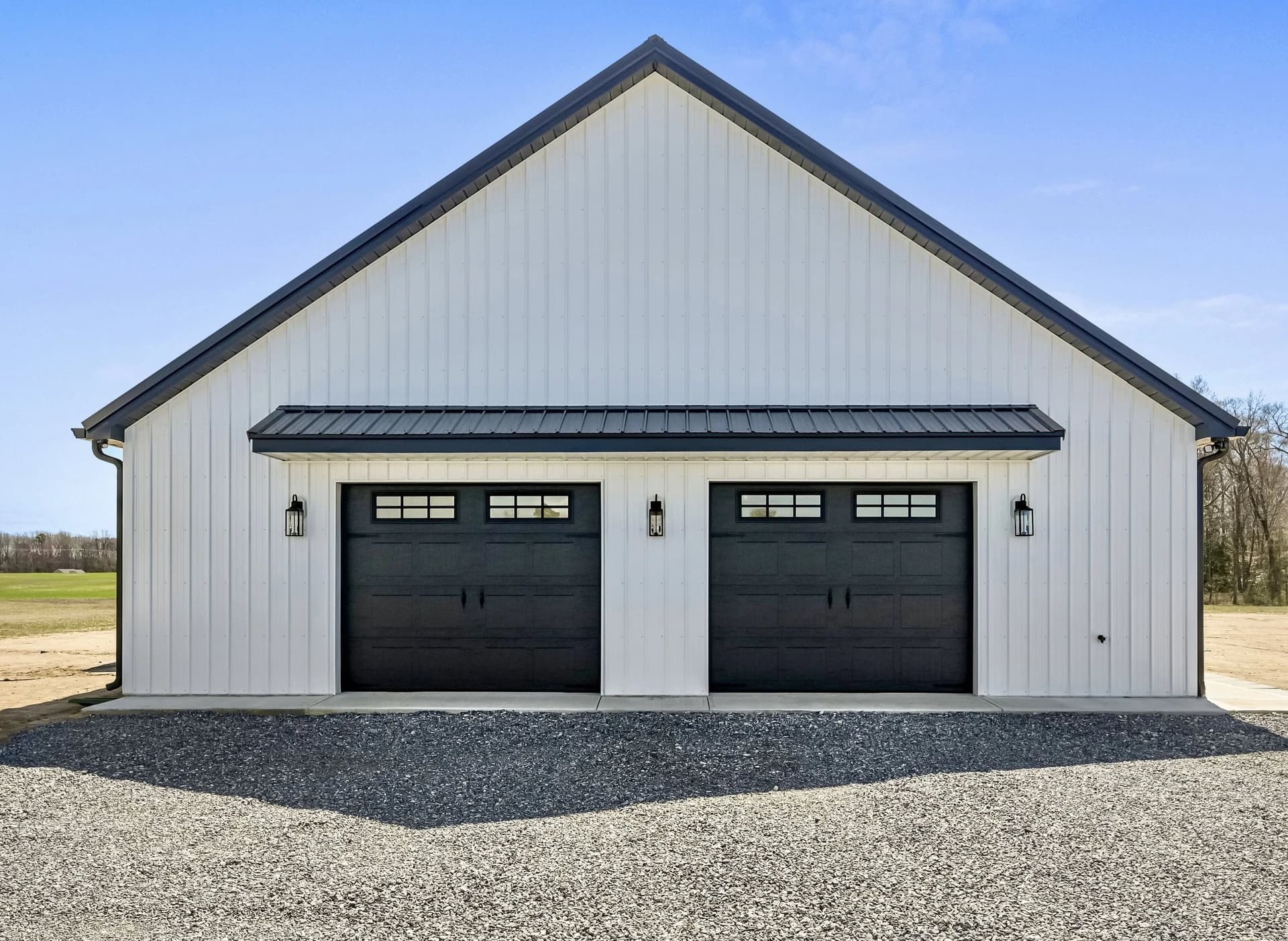 White board-and-batten barn with two black carriage-style garage doors with window tops and lantern lights