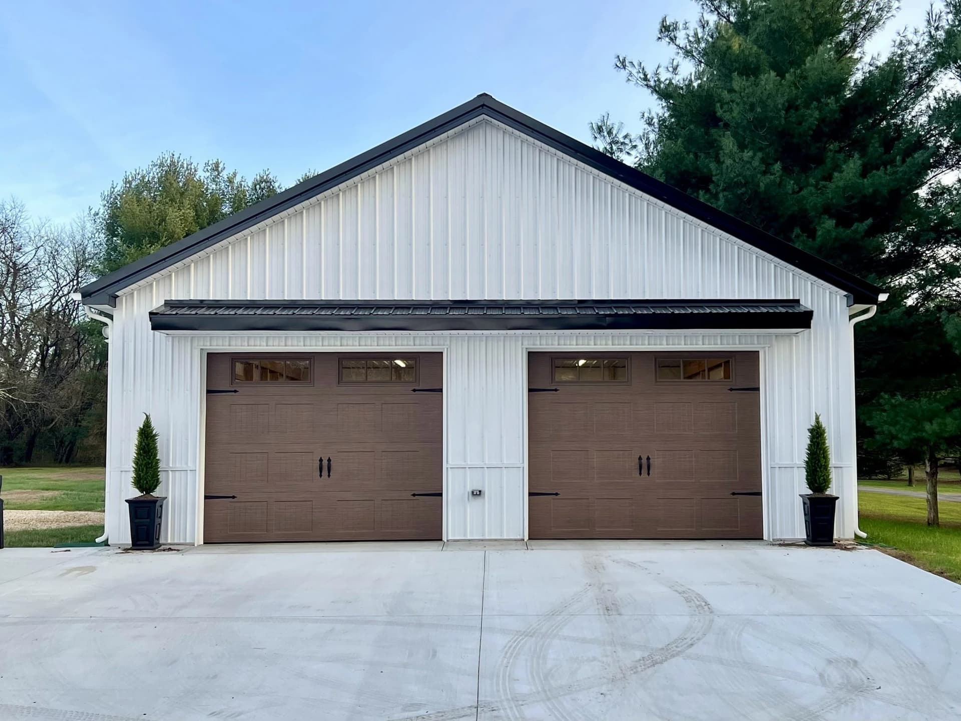 White pole barn with two brown carriage-style garage doors with window tops on a new concrete apron